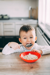 A child in the kitchen eating their own oatmeal with a red plate