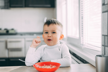 A child in the kitchen eating their own oatmeal with a red plate