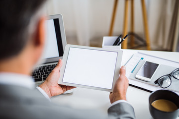 A midsection of businessman sitting at the table, using tablet. A rear view. Copy space.