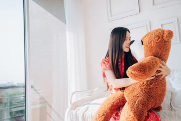 Gift of Asian Chinese New Year Woman Chinese dress,Qipao,Cheongsam hug Bear Sitting on Bed near Window in Clean White Room.