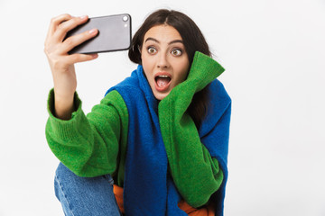 Image of optimistic woman 30s in colorful clothes sitting on the floor and taking selfie on...