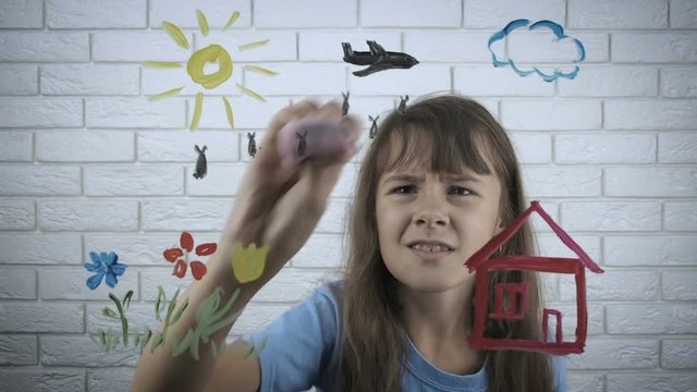 Child against war. A sad little girl wipes an airplane with bombs from her drawing.