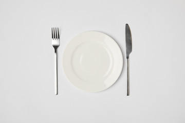 top view of porcelain plate with fork and knive on grey background