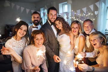 A young bride, groom and guests posing for a photograph on a wedding reception. - obrazy, fototapety, plakaty