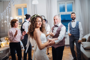 A young bride dancing with grandfather and other guests on a wedding reception.