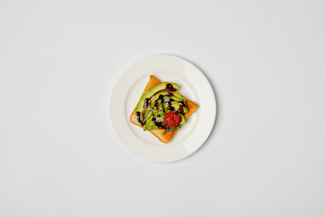 top view of toast in plate with avocado and cherry tomato on grey background
