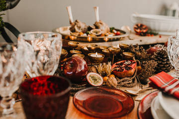 .Detail photograph of a table prepared and decorated for a party diner. Autumnal and festive decoration, with wood pineapples, candles, fruits and red colors. Lifestyle. Food photography