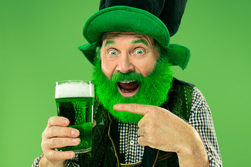 A smiling happy senior man in a leprechaun hat with green beer at studio. He celebrates St....