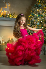 Beautiful little girl in a red dress standing near the New Year tree