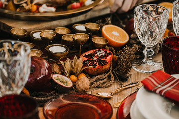 .Detail photograph of a table prepared and decorated for a party diner. Autumnal and festive decoration, with wood pineapples, candles, fruits and red colors. Lifestyle. Food photography
