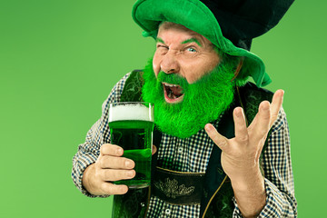 A smiling happy senior man in a leprechaun hat with green beer at studio. He celebrates St....