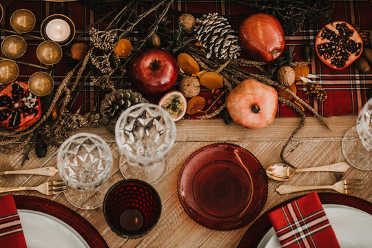 .Detail photograph of a table prepared and decorated for a party diner. Autumnal and festive decoration, with wood pineapples, candles, fruits and red colors. Lifestyle. Food photography