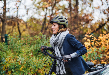 Active senior woman with electrobike cycling outdoors in park.