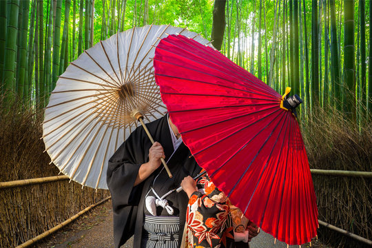 Couple with traditional japanese umbrellas posing at bamboo forest in Arashiyama