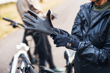 A midsection of active senior couple standing outdoors with electobikes, putting on gloves.