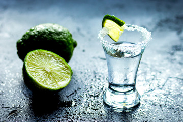 Tequila shot with lime slices and salt on dark background