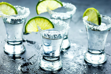 Tequila shot with lime slices and salt on dark background