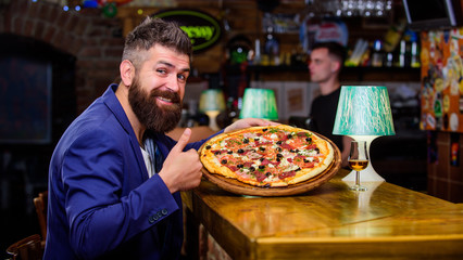 Hipster client sit at bar counter. Man received delicious pizza. Enjoy your meal. Cheat meal concept. Pizza favorite restaurant food. Fresh hot pizza for dinner. Hipster hungry eat italian pizza - obrazy, fototapety, plakaty