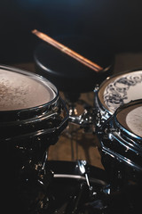 Closeup view of a drum set and Drumsticks in a dark studio. Black drum barrels with chrome trim. The concept of live performances