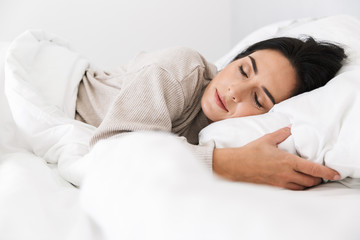 Photo of middle-aged woman 30s sleeping, while lying in bed with white linen at home