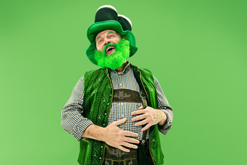 A smiling surprised happy senior man in a leprechaun hat with beard at green studio. He celebrates...