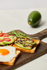 selective focus of wooden cutting board with toasts, scrambled egg, cherry tomatoes and avocado on grey background