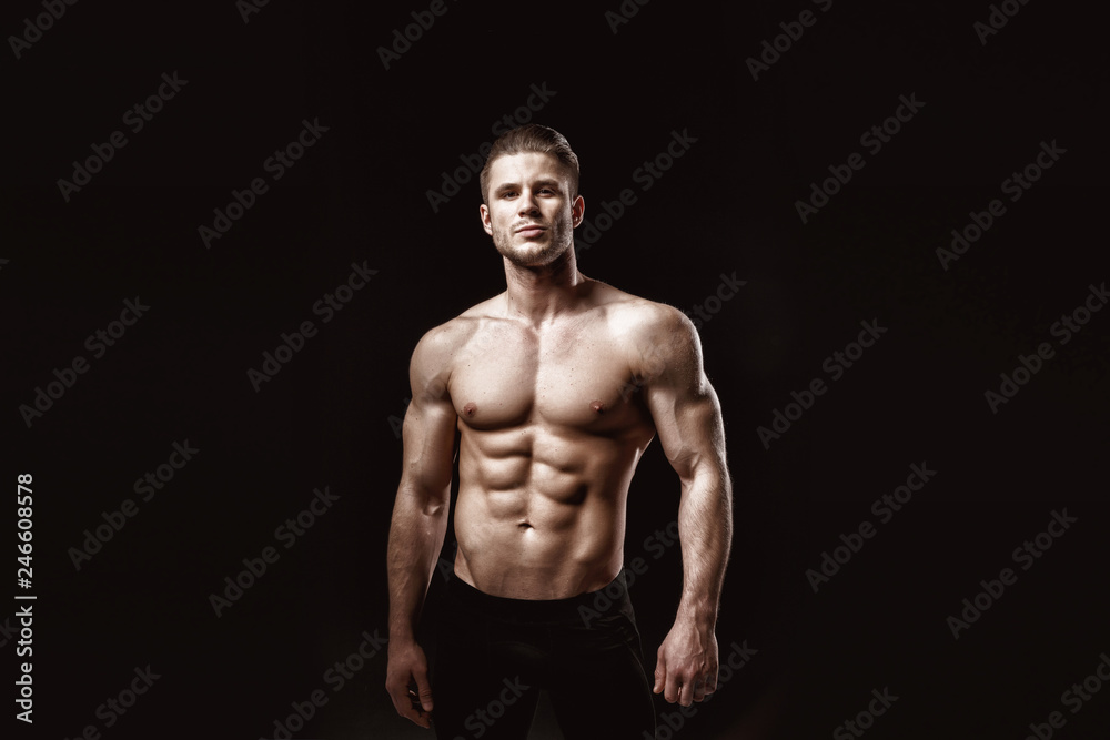 Wall mural Muscular model young man on dark background. Fashion portrait of strong brutal guy with trendy hairstyle. Sexy naked torso, six pack abs. Male flexing his muscles. Sport workout bodybuilding concept.