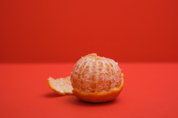 Half peeled Mandarin orange shot on a plain isolated red background.
