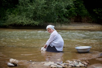 A girl in a long village vintage clothes sitting on the Bank of the river and washes clothes.