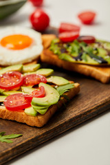 selective focus of cutting board with toasts, scrambled egg, cherry tomatoes and avocado on white background