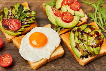 selective focus of toasts with scrambled egg, cherry tomatoes and avocado on wooden background