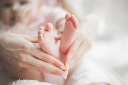 Baby`s feet closeup picture. Mother`s hands holding child`s foot. Little girl`s fingers at front. Background of parenthood.