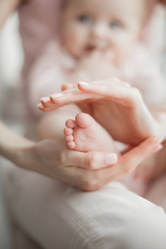 Baby`s feet closeup picture. Mother`s hands holding child`s foot. Little girl`s fingers at front. Background of parenthood.