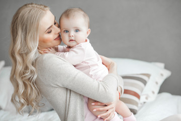 Young mother taking care of her little baby girl. Beautiful mom and her daughter indoors in the...