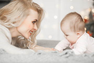 Young mother taking care of her little baby girl. Beautiful mom and her daughter indoors in the bedroom. Loving family. Attractive mum holding her child.
