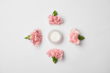 Flat lay of carnations flowers in rhombus arranging and cream container on white background