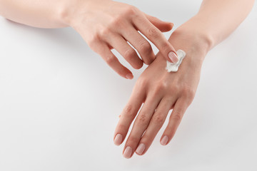Partial view of woman applying cosmetic cream on hands on white background