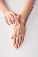 Fototapeta premium Partial view of woman applying cosmetic cream on white background