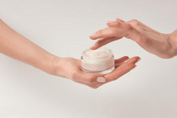 Partial view of woman applying cosmetic cream on white background