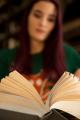 young girl with long hair reading a book on a blurred background of bookshelves in the library
