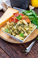 Macaroni with pesto (penne rigate). With onion and bacon, cheese, basil, pine nuts, garlic. On a wooden table with a rustic look.
