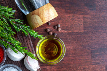Ingredients and spices for roasts (black pepper, olive oil, garlic, fresh rosemary, salt). On dark wood background.Top view.