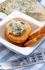 Blue cheese (Cabrales) spread on toasted bread. Includes a spread knife and block of cheese on a plate.