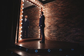 Elegant look. Full length of handsome man in full suit adjusting his jacket while standing in front of the mirror indoors © opolja