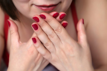 Manicure and makeup, female cosmetics, beauty shop. Perfect hands with red nail polish, part of smiling woman's face with red lips, selective focus