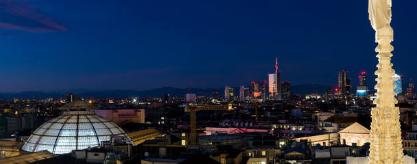 Aerial view of Milan skyline by night from Duomo (cathedral) roof. Spire in the foreground and skyscrapers of the Porta Nuova district in the background.