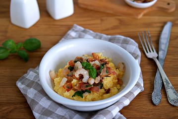 Homemade shrimp and grits with bacon, Chedder cheese and parsley in a white bowl on a wooden table.