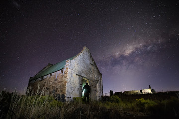 Wide angle astrophotography scene of an old abandoned building with the bright nigh sky above it.