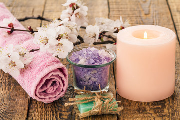 Fototapeta na wymiar Soap, sea salt in glass bowl with towel for bathroom procedures and burning candle with flowering branch of apricot tree