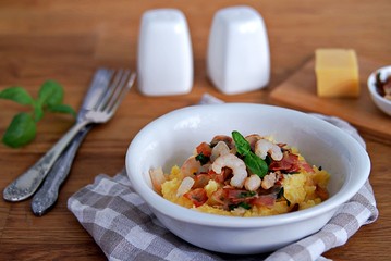 Homemade shrimp and grits with bacon, Chedder cheese and parsley in a white bowl on a wooden table.
